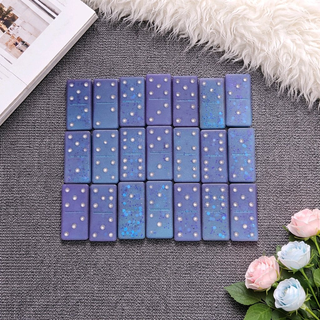 Set of blue dice with star patterns on a gray surface with flowers and a book in the background