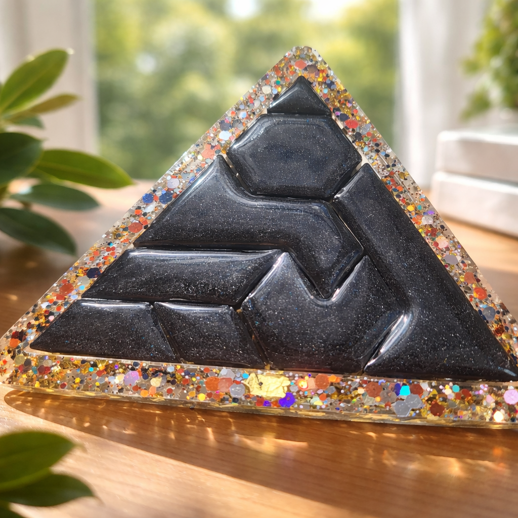 Decorative pyramid with multicolored base and black geometric design on a wooden surface.