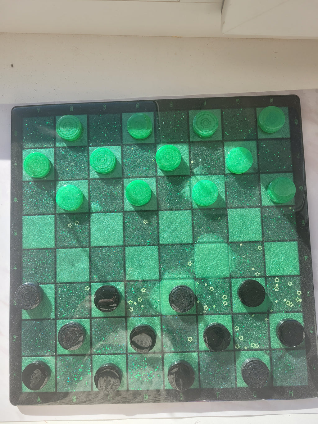 Checkers board with green and black pieces on a white background