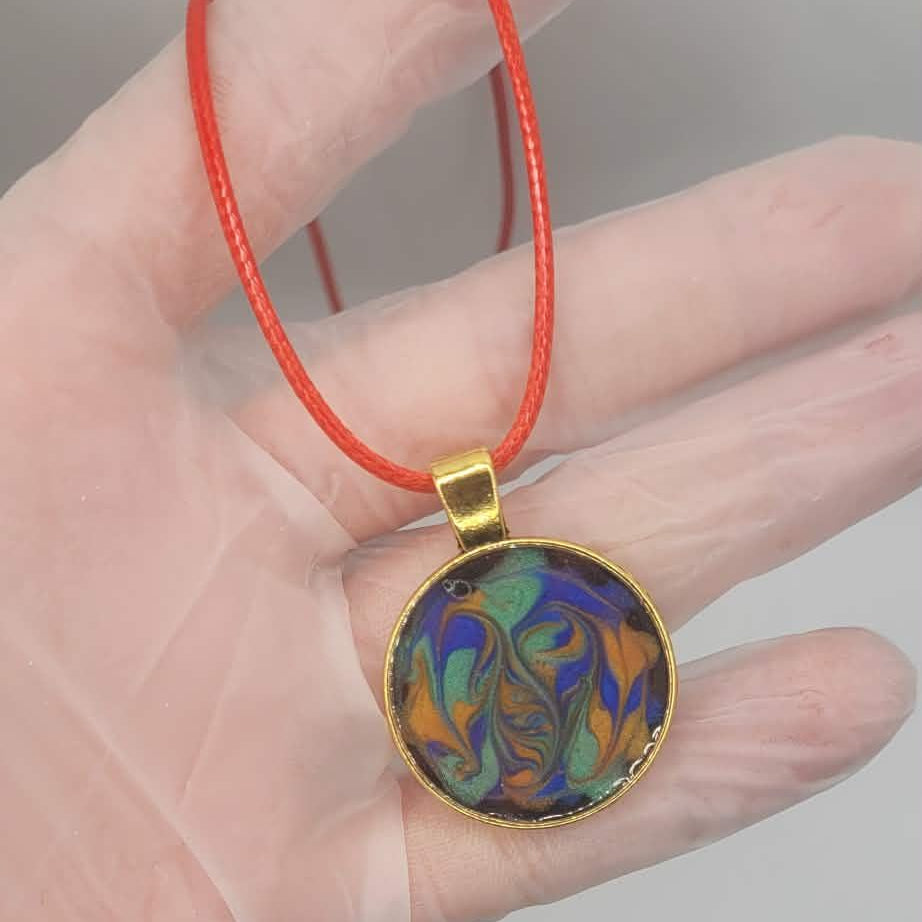 Colorful pendant on a red string held in a hand against a neutral background