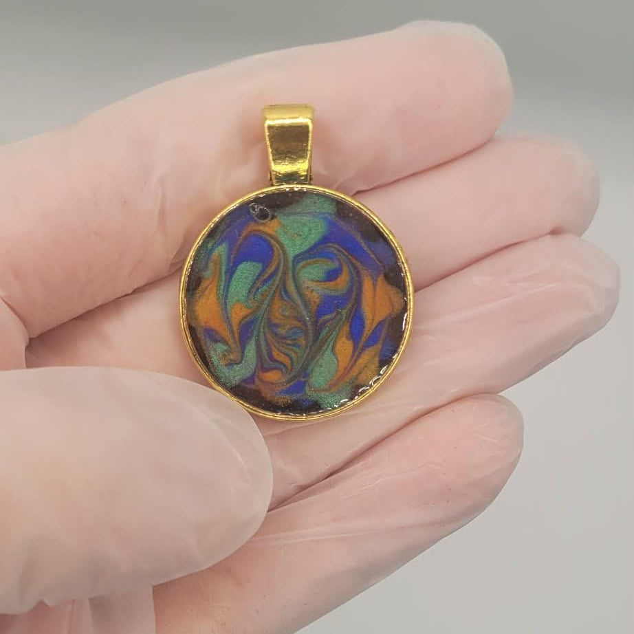 Hand holding a colorful pendant with a gold frame against a plain background