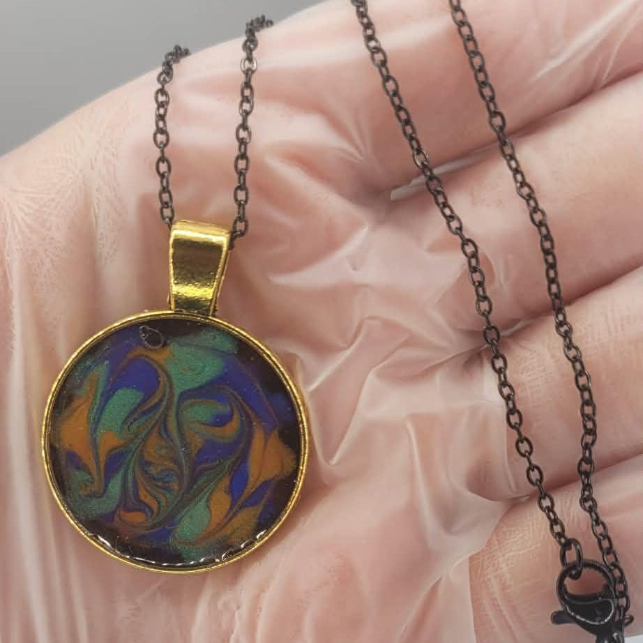 Black necklace with a colorful pendant held in a hand against a neutral background