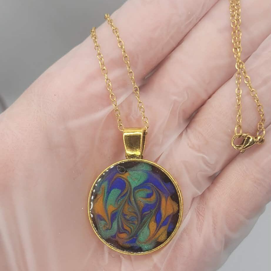 Gold necklace with a colorful pendant held in a hand against a neutral background