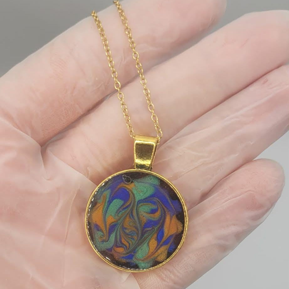 Colorful pendant on a gold chain held in a hand against a neutral background
