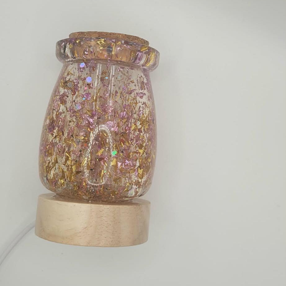 Decorative jar with glittery contents on a wooden base against a plain background