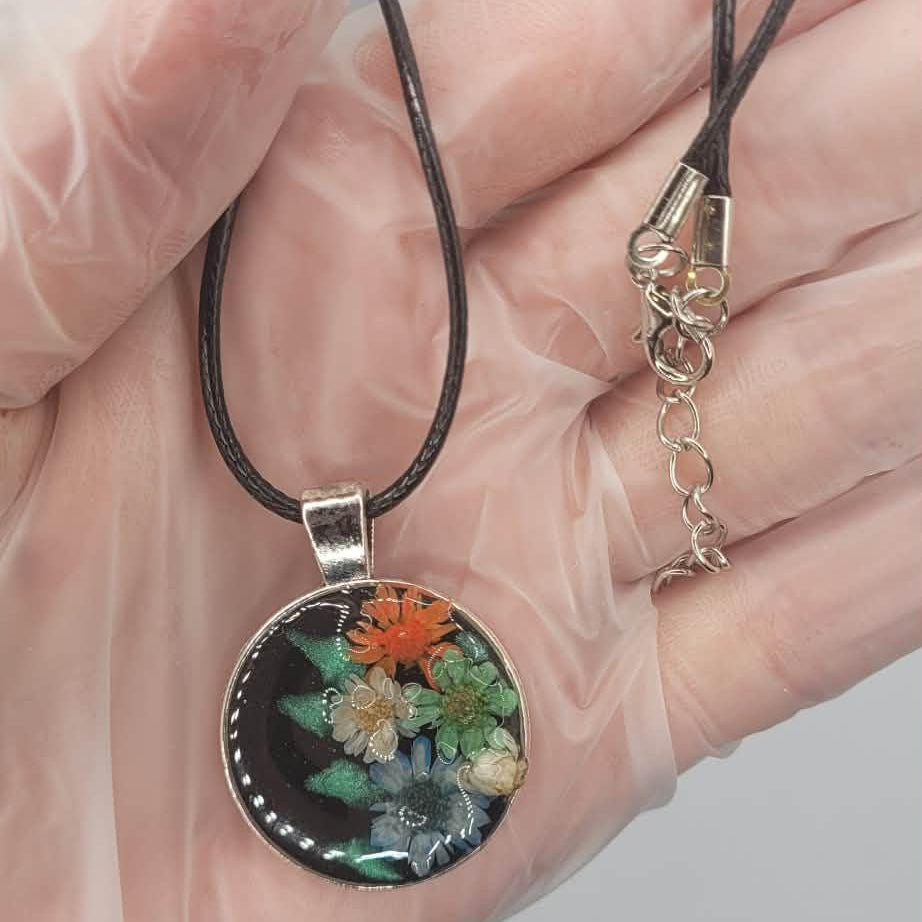 Hand holding a floral pendant necklace with a clear background