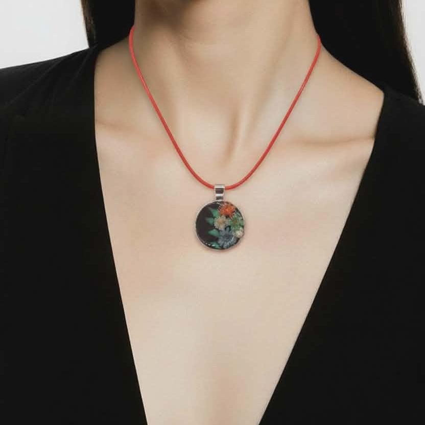 Person wearing a black top with a red necklace featuring a floral pendant.