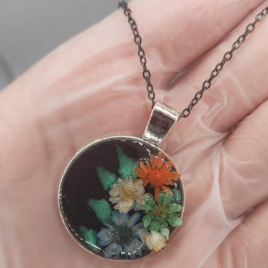 Necklace with a real dried floral pendant held in a hand against a neutral background