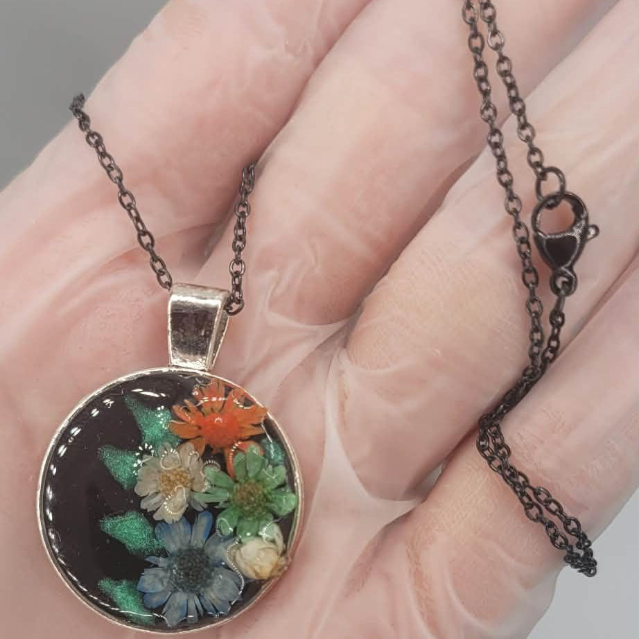 Necklace with a real dried floral pendant held in a hand against a neutral background