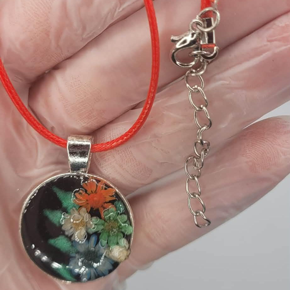Hand holding a necklace with a pendant featuring floral design on a red cord against a neutral background