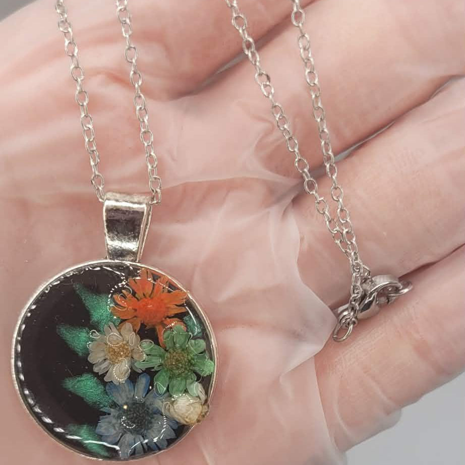 Necklace with a real birth flower pendant held in a hand against a neutral background