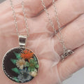 Necklace with a real birth flower pendant held in a hand against a neutral background