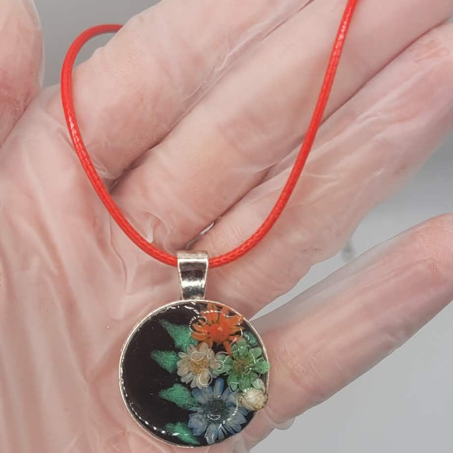Hand holding a floral pendant on a red string against a neutral background