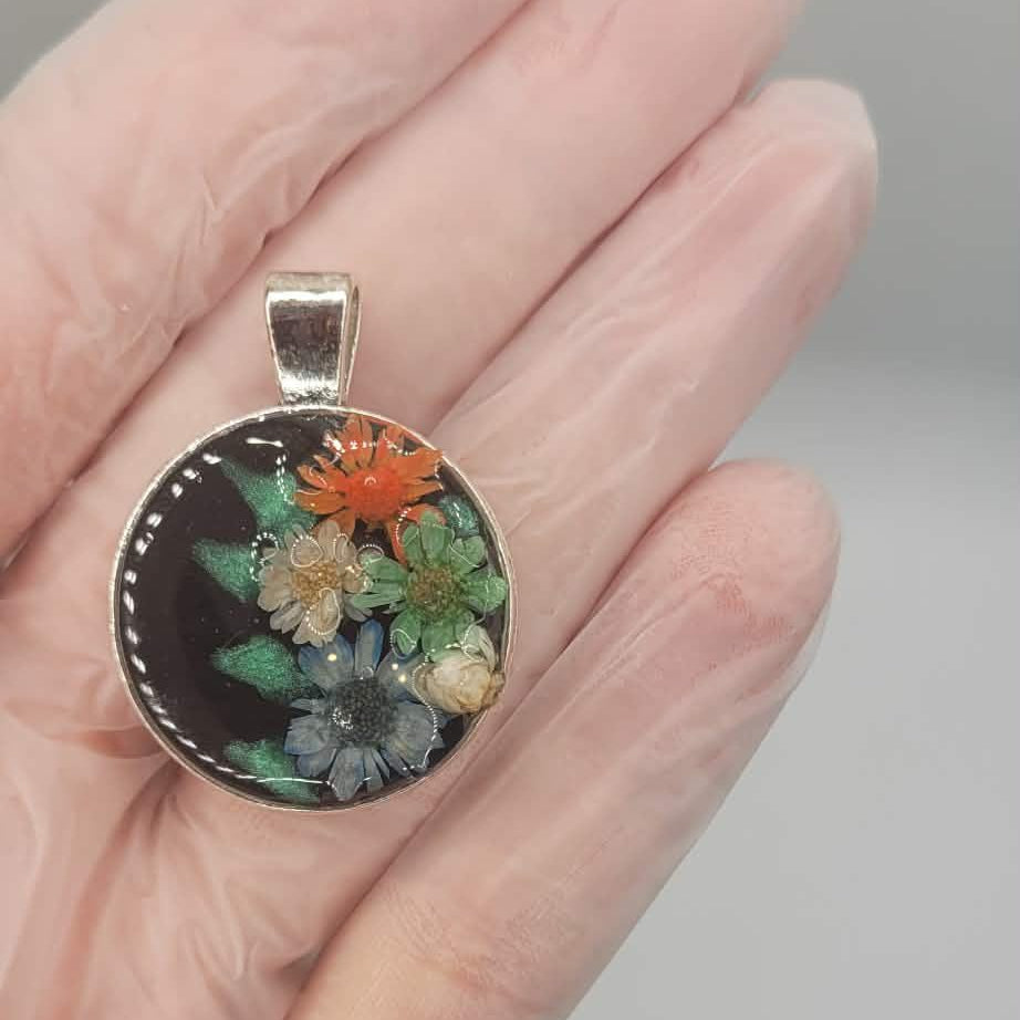 Floral pendant held in a hand against a neutral background