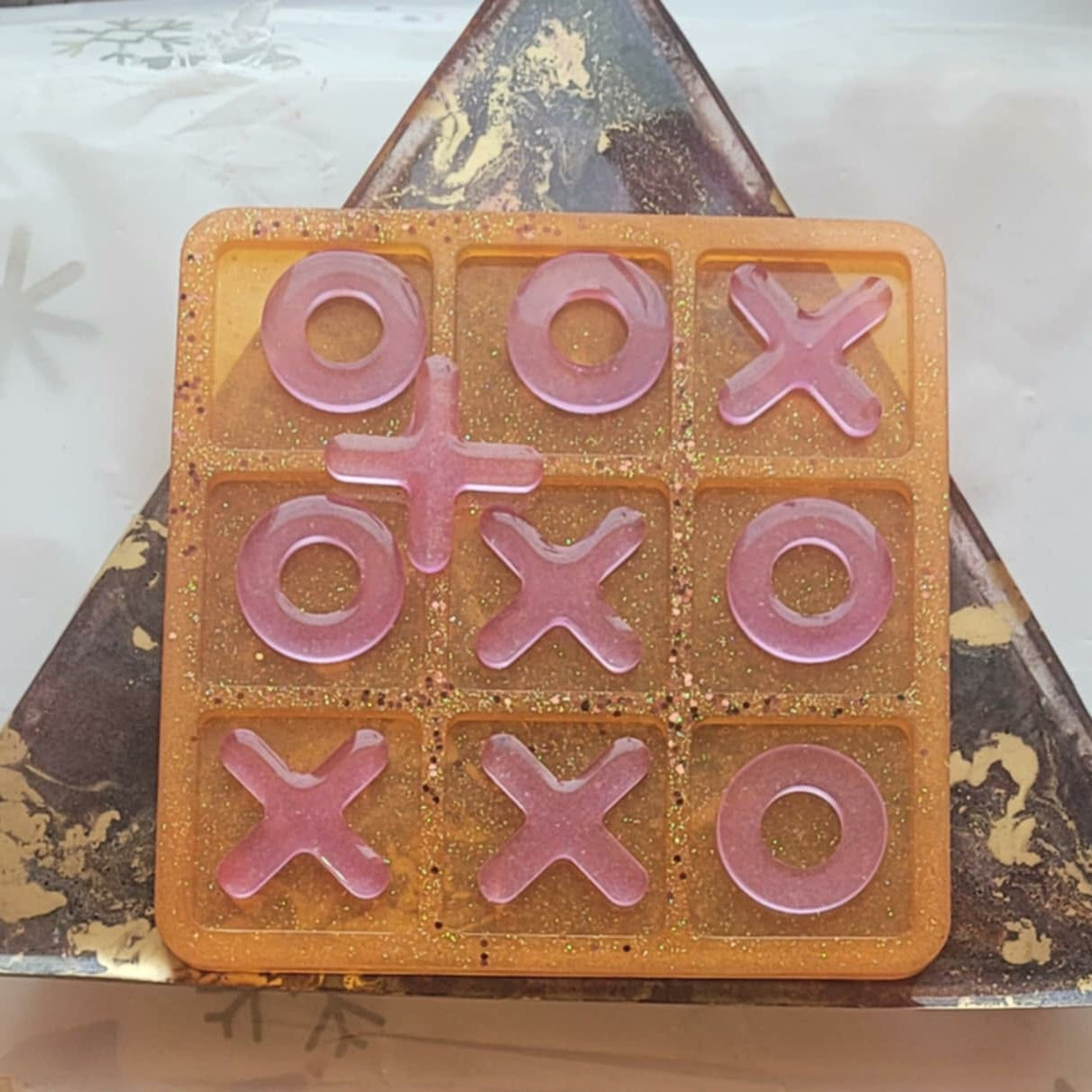 Tic-tac-toe game set with pink pieces on a decorative stone surface