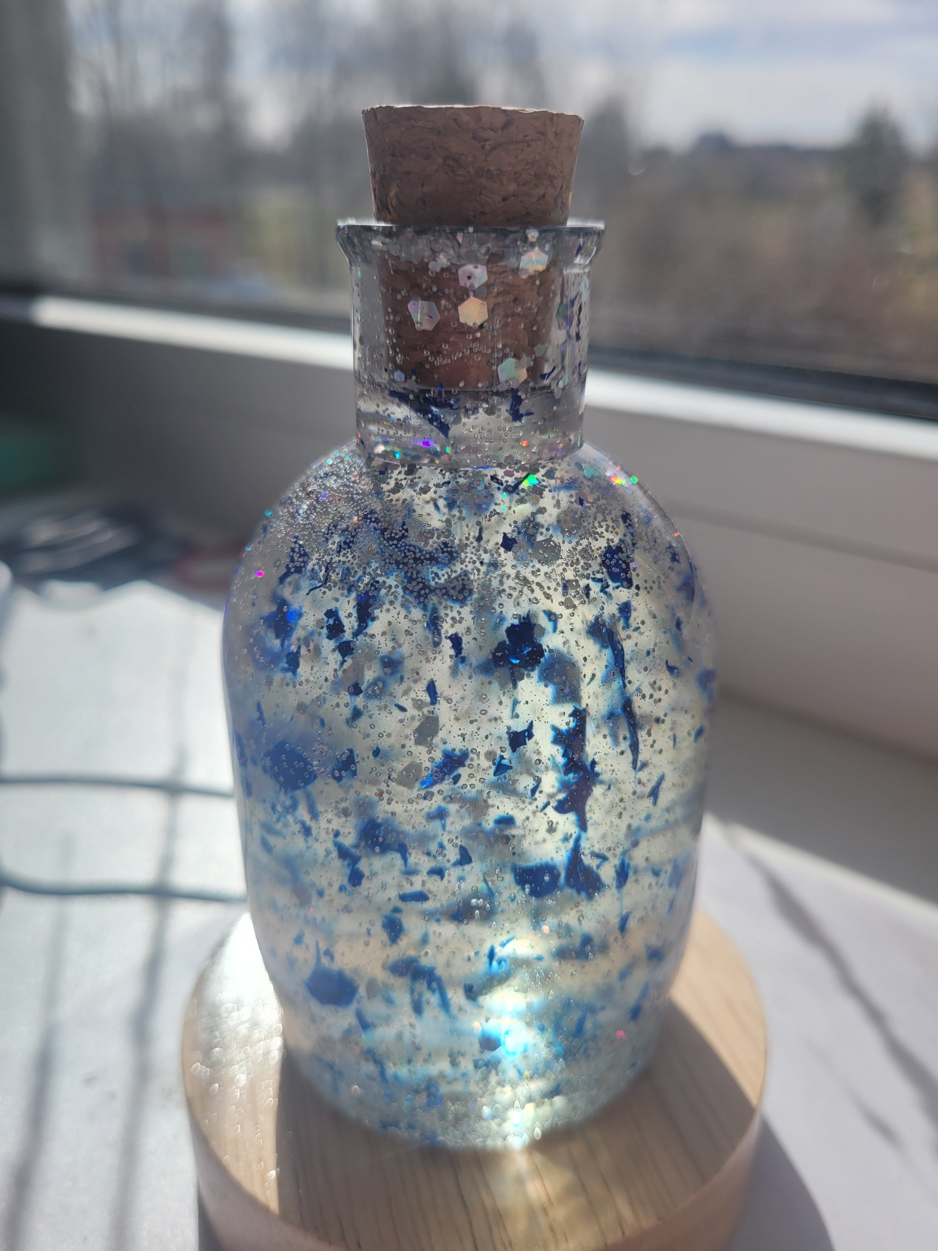 Decorative bottle with glittery contents held by a hand against a blurred background