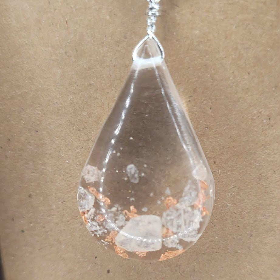 Teardrop-shaped pendant with embedded himalayan stones on a black cord against a brown background